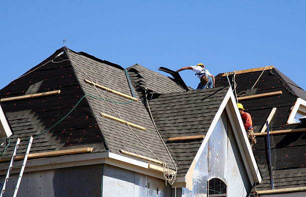 Workers installing new roof shingles against blue sky